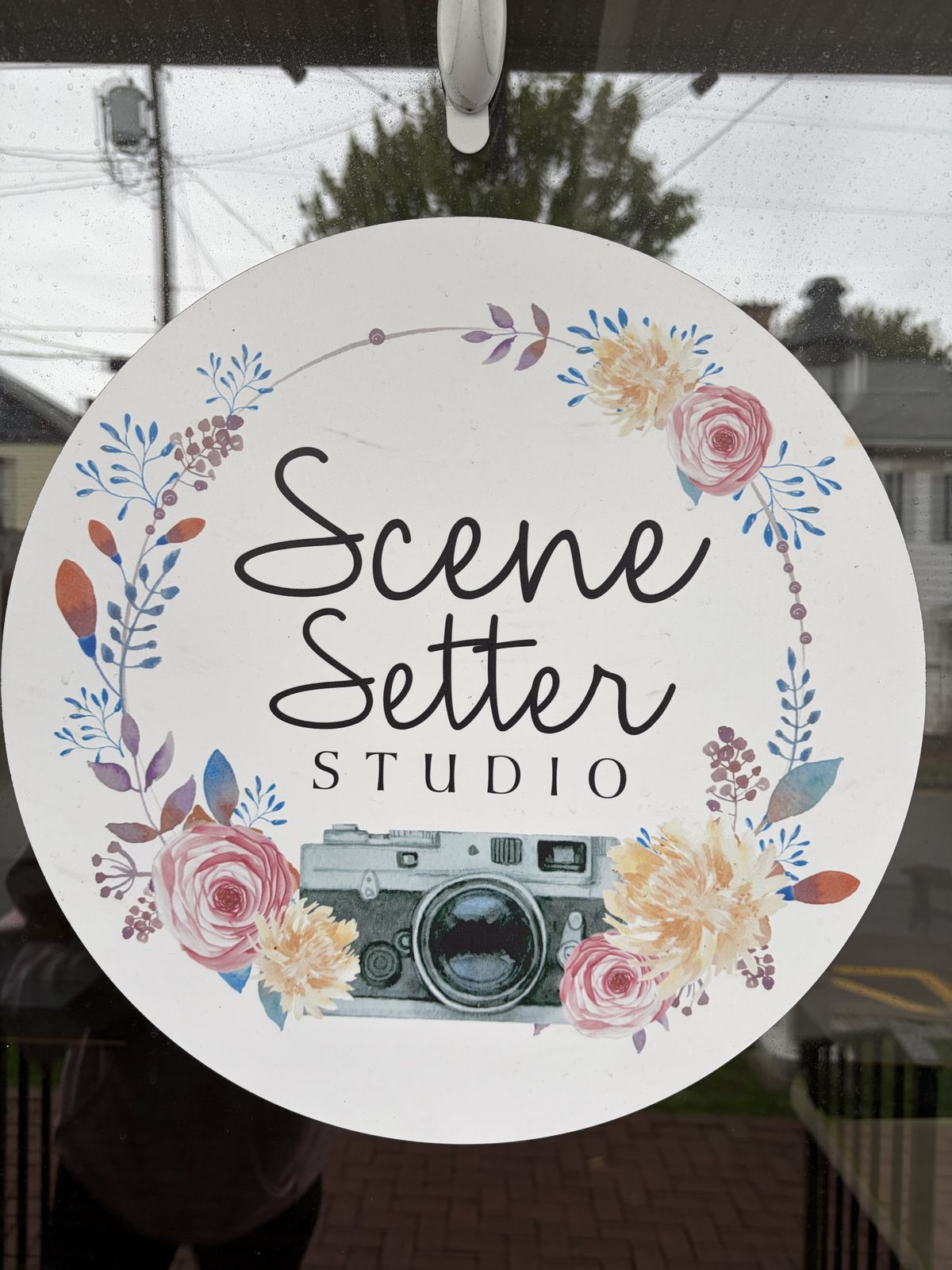 The Scene Setter Studio floral logo sign hanging in the front window